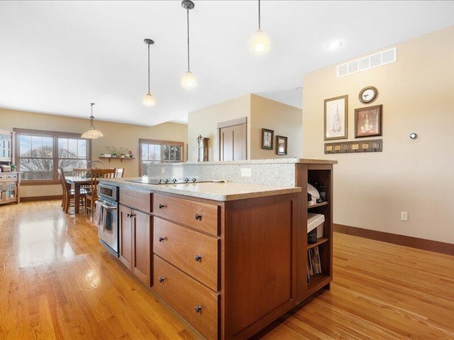 kitchen with visible vents, brown cabinets, decorative light fixtures, oven, and light wood-style floors