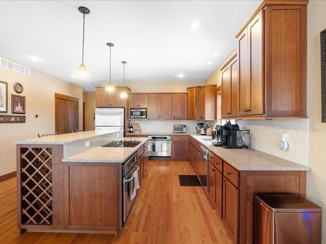 kitchen with brown cabinetry, a breakfast bar area, light stone counters, stainless steel appliances, and pendant lighting