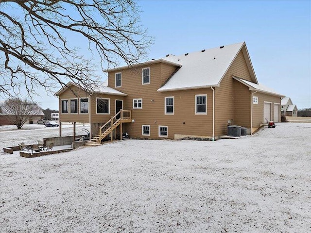 snow covered back of property featuring stairs, a garage, and central air condition unit