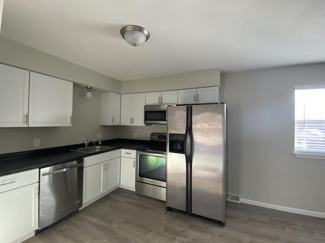 kitchen featuring white cabinets, dark countertops, stainless steel appliances, and a sink