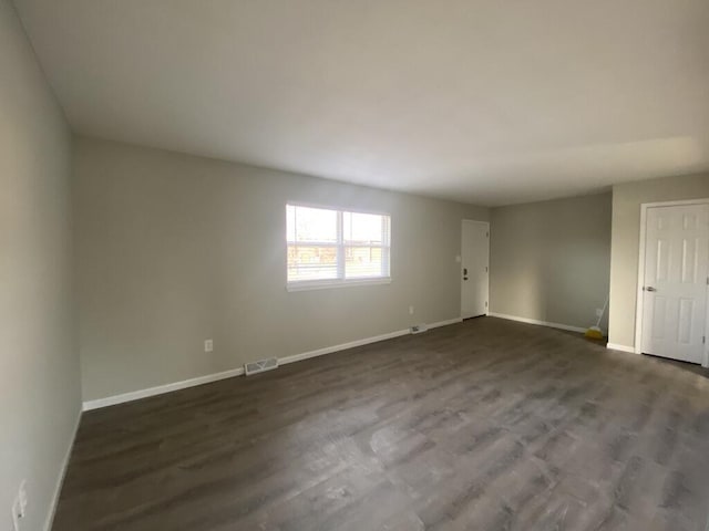 empty room with dark wood-style flooring, visible vents, and baseboards