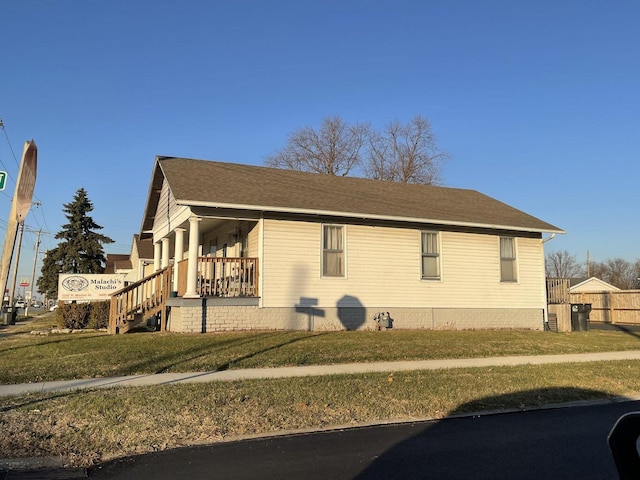 view of side of home featuring covered porch, roof with shingles, and a lawn