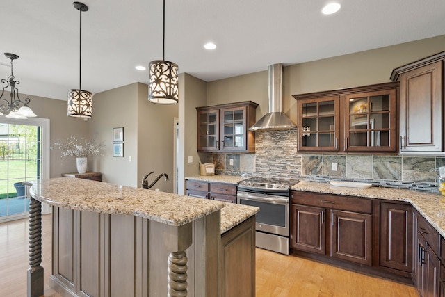 kitchen featuring light wood-style floors, stainless steel range with electric cooktop, backsplash, wall chimney exhaust hood, and pendant lighting