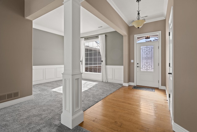 carpeted entrance foyer featuring visible vents, ornamental molding, wainscoting, wood-type flooring, and decorative columns