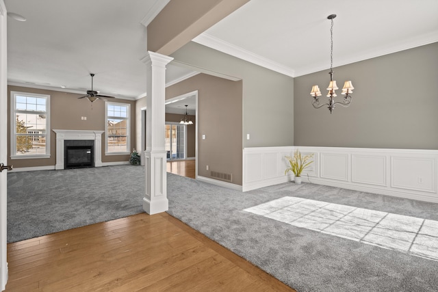 unfurnished dining area with crown molding, visible vents, a fireplace with flush hearth, ornate columns, and ceiling fan with notable chandelier