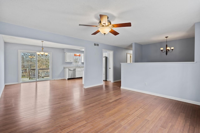 unfurnished living room with ceiling fan with notable chandelier, visible vents, baseboards, and wood finished floors