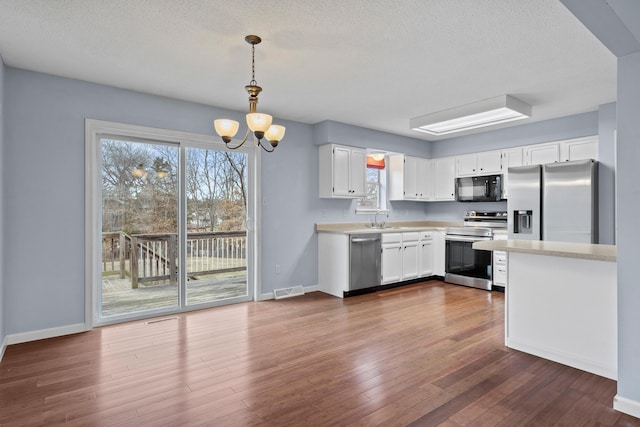 kitchen with dark wood finished floors, a notable chandelier, light countertops, appliances with stainless steel finishes, and white cabinets