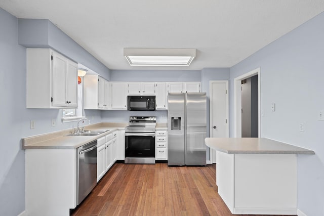 kitchen with white cabinets, appliances with stainless steel finishes, wood finished floors, light countertops, and a sink