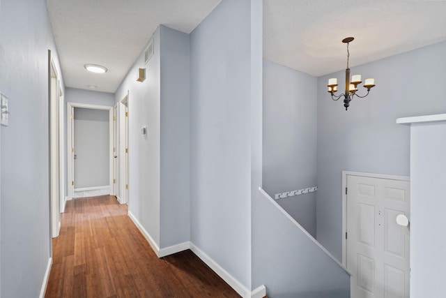 corridor featuring a textured ceiling, wood finished floors, an upstairs landing, baseboards, and an inviting chandelier