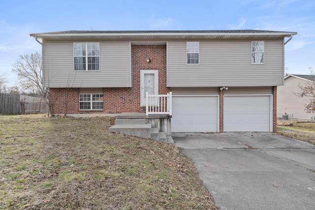 split foyer home featuring an attached garage, brick siding, fence, driveway, and a front yard