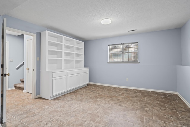 unfurnished room featuring visible vents, a textured ceiling, baseboards, and stairs