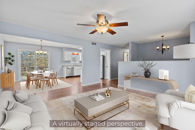 living area with baseboards, ceiling fan with notable chandelier, visible vents, and light wood-style floors