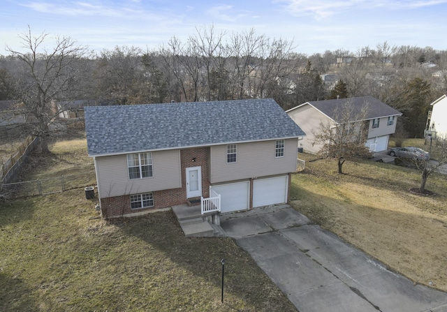 split foyer home featuring an attached garage, roof with shingles, concrete driveway, and brick siding