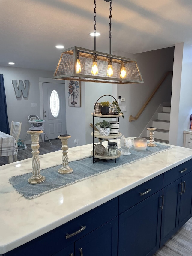 kitchen with blue cabinetry, decorative light fixtures, light stone counters, and light wood-type flooring