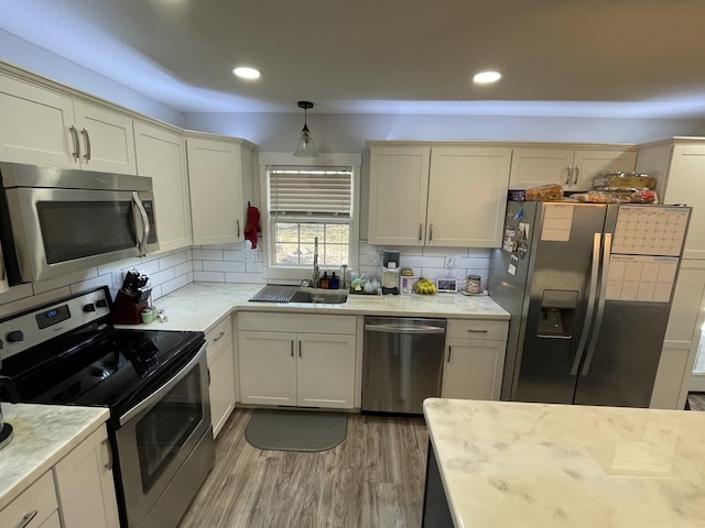 kitchen with a sink, decorative backsplash, light wood finished floors, and stainless steel appliances