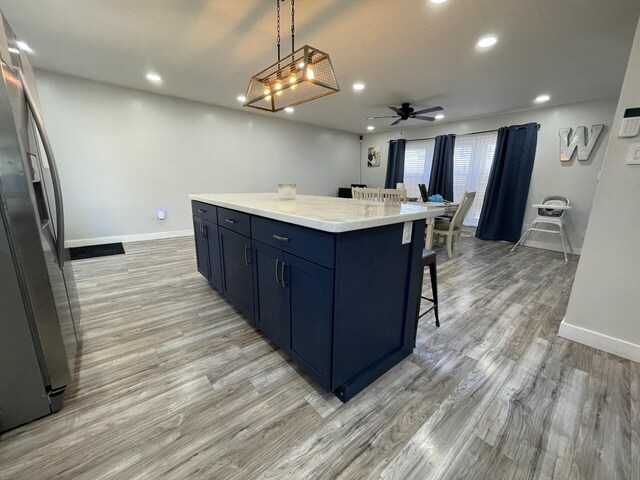 kitchen featuring a breakfast bar, freestanding refrigerator, recessed lighting, light wood-style floors, and baseboards