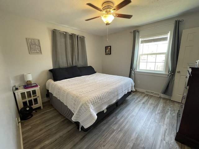 bedroom with a ceiling fan, visible vents, wood finished floors, and baseboards