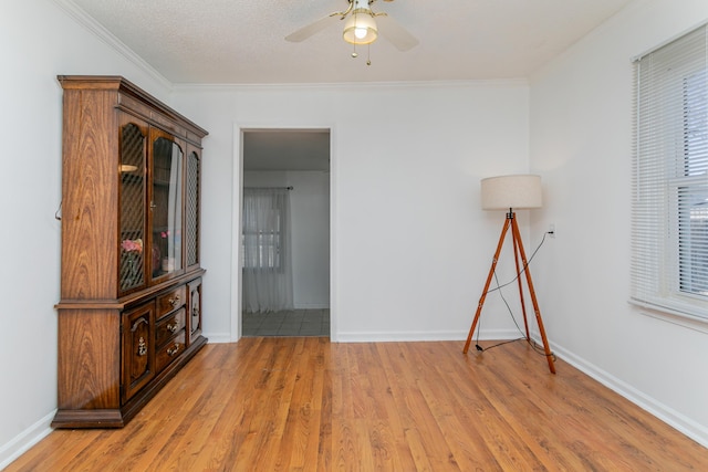 spare room with light wood-style flooring, ornamental molding, ceiling fan, and baseboards