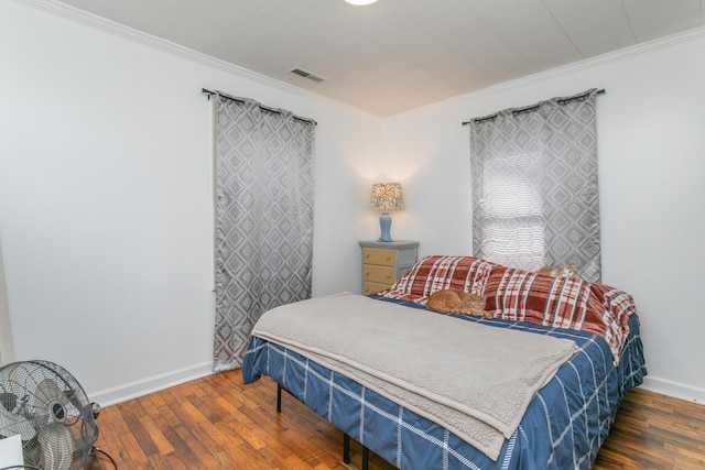 bedroom with hardwood / wood-style floors, baseboards, visible vents, and crown molding