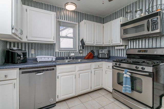 kitchen featuring stainless steel appliances, a sink, white cabinets, dark countertops, and wallpapered walls