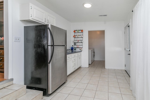 kitchen featuring washing machine and clothes dryer, light tile patterned floors, visible vents, freestanding refrigerator, and white cabinets