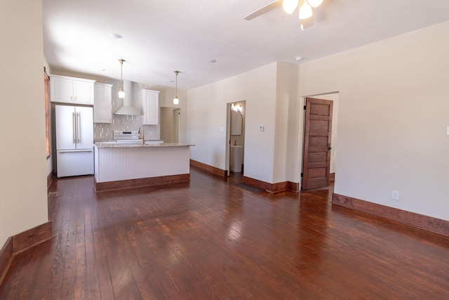 kitchen featuring an island with sink, dark wood-type flooring, freestanding refrigerator, wall chimney range hood, and white cabinetry