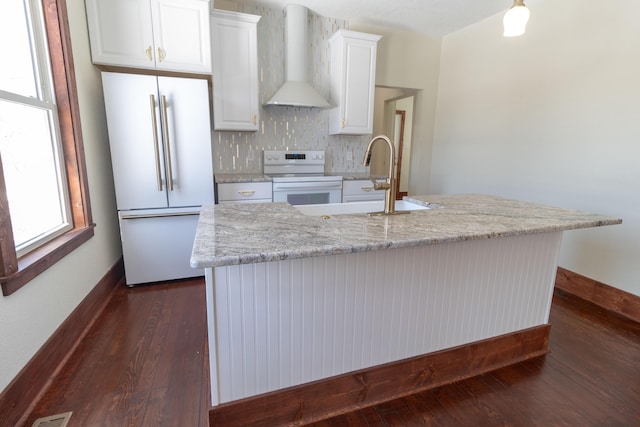 kitchen with white appliances, dark wood-style floors, wall chimney exhaust hood, white cabinetry, and a sink