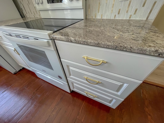 kitchen with electric range, white cabinets, backsplash, light stone countertops, and dark wood-style floors