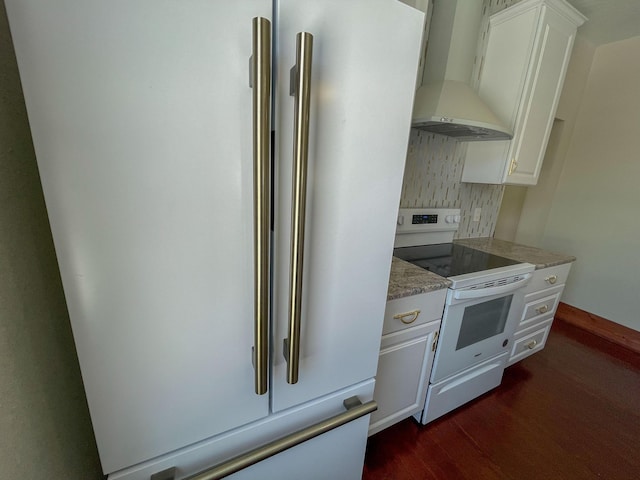 kitchen with high end refrigerator, white cabinets, wall chimney exhaust hood, white range with electric cooktop, and dark wood finished floors