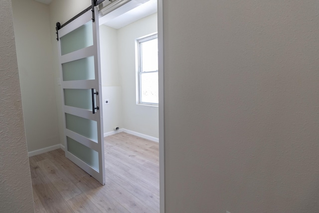 corridor featuring light wood-type flooring, baseboards, and a barn door