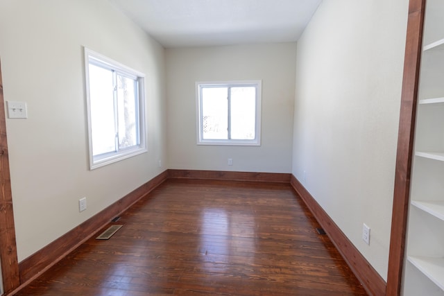 empty room featuring baseboards, plenty of natural light, visible vents, and dark wood-style flooring