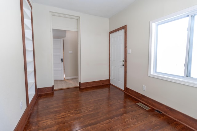 spare room featuring dark wood-type flooring, visible vents, and baseboards