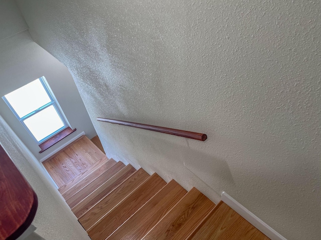 stairway with a textured wall, baseboards, and wood finished floors