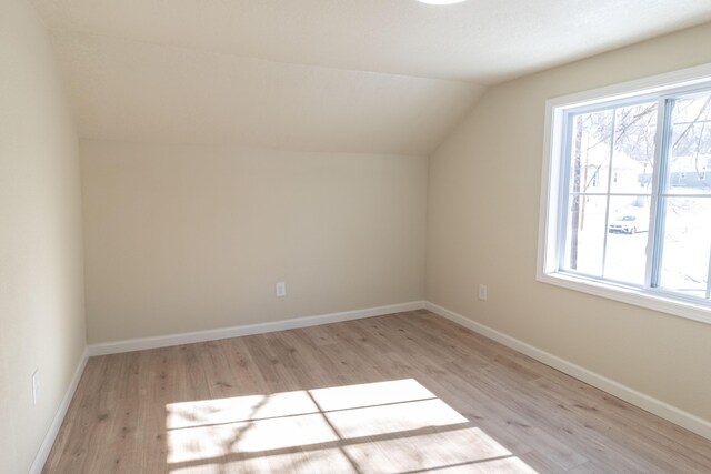 additional living space featuring lofted ceiling, baseboards, a wealth of natural light, and light wood-style floors