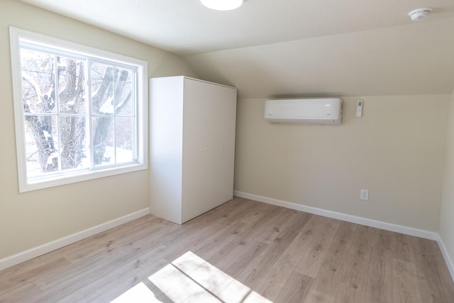 additional living space featuring vaulted ceiling, an AC wall unit, light wood finished floors, and baseboards