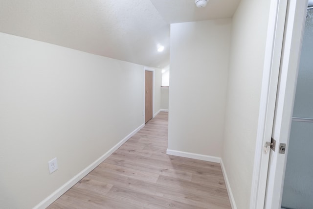 hallway featuring vaulted ceiling, light wood-type flooring, and baseboards