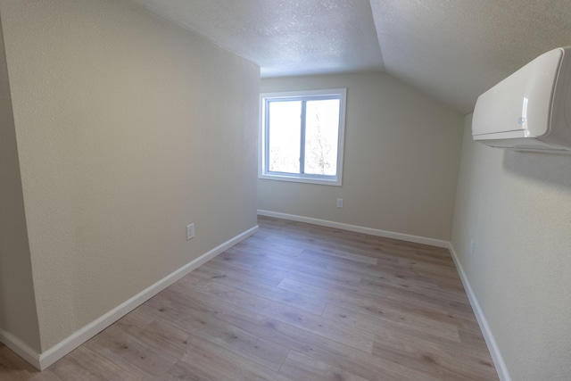 additional living space featuring a wall unit AC, light wood-type flooring, vaulted ceiling, and a textured ceiling