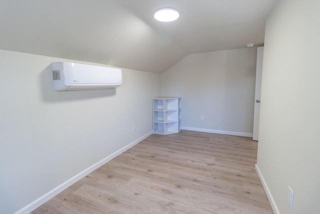 additional living space featuring lofted ceiling, light wood-type flooring, a wall mounted air conditioner, and baseboards