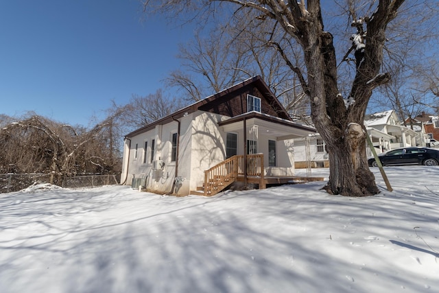 view of snowy exterior featuring covered porch and brick siding