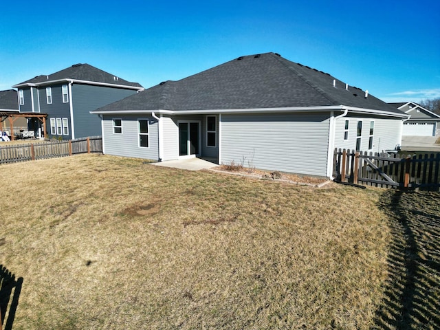 back of house with a shingled roof, a fenced backyard, a lawn, and a patio