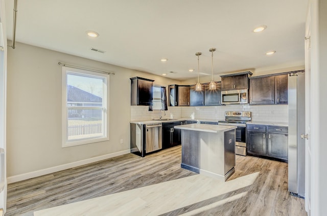 kitchen with stainless steel appliances, light countertops, hanging light fixtures, backsplash, and a kitchen island