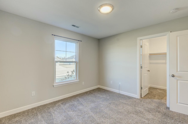 unfurnished bedroom featuring a closet, visible vents, a spacious closet, light carpet, and baseboards