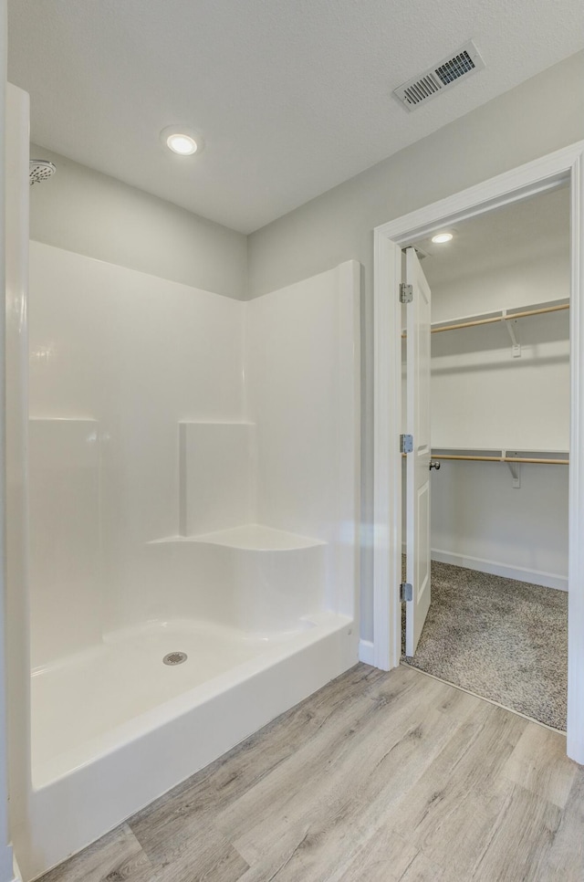 full bath featuring a spacious closet, visible vents, a shower, and wood finished floors