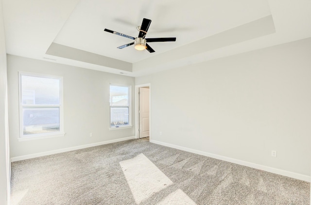 carpeted empty room with baseboards, a tray ceiling, and ceiling fan