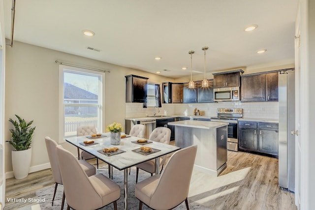 kitchen with a center island, light countertops, hanging light fixtures, appliances with stainless steel finishes, and dark brown cabinets