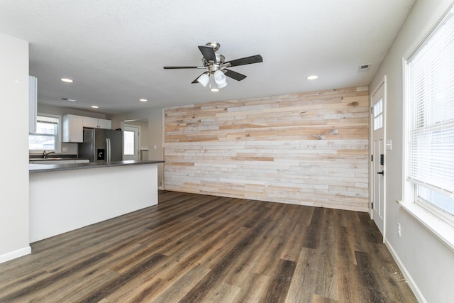 unfurnished living room featuring wood walls, an accent wall, baseboards, and dark wood finished floors