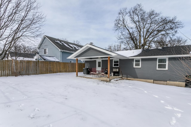 snow covered back of property with covered porch, brick siding, and fence