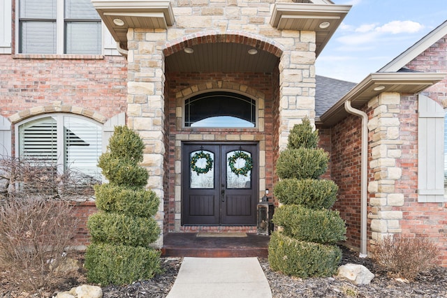 doorway to property with stone siding, a shingled roof, french doors, and brick siding