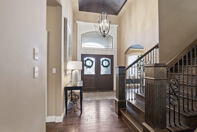 foyer with high vaulted ceiling, baseboards, stairs, hardwood / wood-style floors, and an inviting chandelier