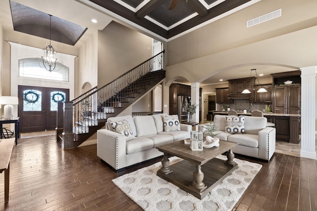 living room with arched walkways, dark wood-style flooring, visible vents, coffered ceiling, and ornate columns